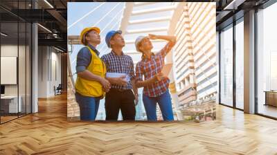 Three industrial engineer wear safety helmet and holding tablet engineering working and talking with drawings inspection on building outside. Engineering tools and construction concept. Wall mural