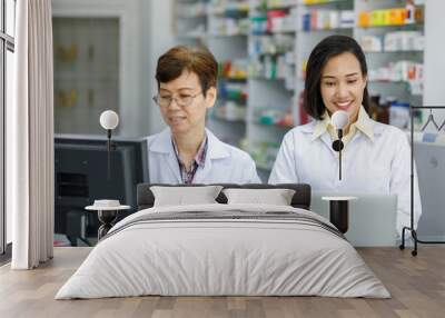 2 female asian pharmacist in white uniforms are keying drug information on laptop compute Wall mural