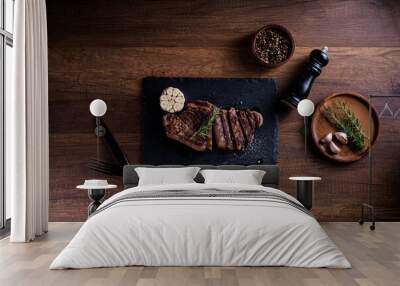 Sliced striploin steak, grillid with 4seasons pepper garlic rosemary, on stone plate dark and wooden background , knife and fork black, top view Wall mural