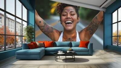 A young woman with tattoos smiles and raises her arms in the air. Wall mural