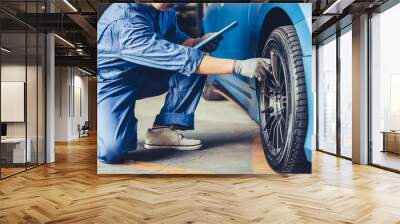 Asian car mechanic technician holding clipboard and checking to maintenance vehicle by customer claim order in auto repair shop garage. Wheel tire repair service. People occupation and business job Wall mural