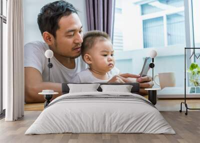 Asian father and son using smart phone together in home background. Technology and People concept. Lifestyles and Happy family theme. Internet and communication theme Wall mural