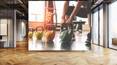 Close up of woman lifting kettlebell like dumbbells in fitness sport club gym training center with sport equipment near window background. Lifestyles and workout exercise for bodybuilding and healthy Wall mural