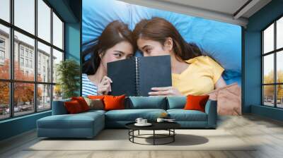 Cute Asian lesbian couple reading book together and lying on bed. Lifestyles and lovers concept. Happiness life and relax theme. Wall mural