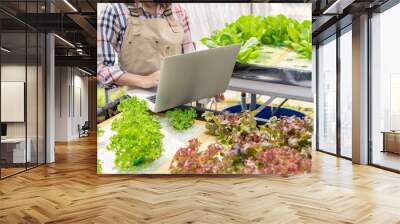 Hydroponic female farmer collecting vegetable growth information and using laptop for upload data to customer for online trading internet for sale. Technology and modern business communication concept Wall mural