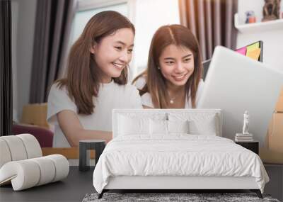 Two young Asian girl teamwork in freelance do small business with laptop to check order, online shopping and marketing. Packaging business and Small business concept Wall mural