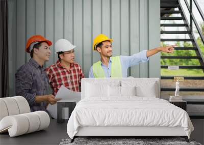 engineer and construction team holding blueprint on hand and pointing finger to building. they are checking construction process in construction site area. Wall mural