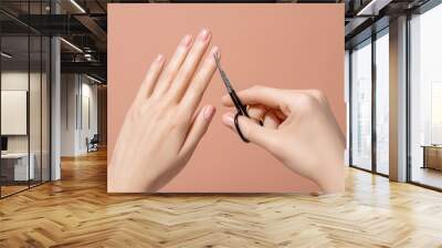 Hands holding a manicure scissors against neutral beige background. Self made manicure. Fingernail, hand care at home concept. Image for beauty salon, cosmetologist or manicure artist promotion. Wall mural