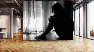 black and white of sad woman hug her knee and cry. Sad woman sitting alone in a empty room beside window or door Wall mural