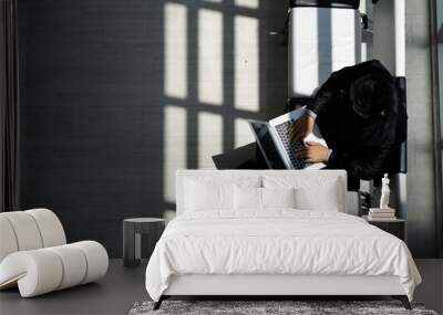 Top view of business man typing on laptop sitting in a chair by the window in the office with sun light cast rhythm of shadow on the floor. Wall mural