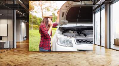 Young woman standing on the side of the road with broken car and calls the evacuation service. Wall mural