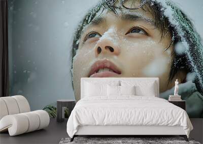 Close-up of a young man's face covered in snowflakes as he looks up at the falling snow. Wall mural