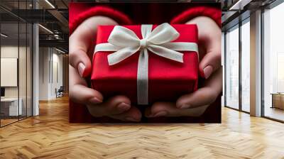 Close-up of hands holding a red gift box with a white bow. Wall mural