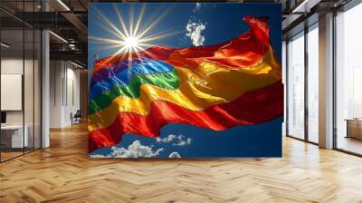 Rainbow flag waving in the wind, with a bright sun shining in the background. Wall mural