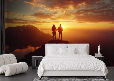 Silhouetted couple holding hands at sunset on a mountain peak. Wall mural