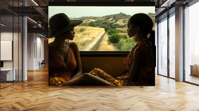 Two women in yellow dresses sit facing each other on a train, looking out the window at the countryside. Wall mural