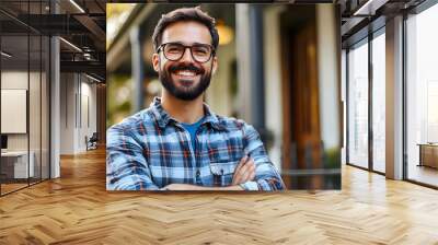 A happy man with a beard and glasses, wearing a plaid shirt, smiles in front of a house. Wall mural