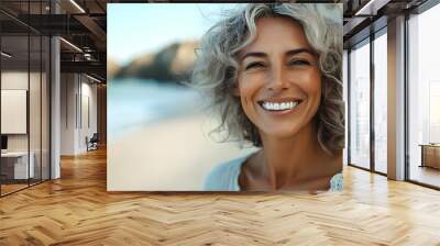 A smiling woman with curly hair on a beach. Wall mural