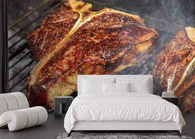 Selection of meat and vegetables grilling on a portable summer barbecue outdoors with focus to a succulent lean t-bone steak with rosemary seasoning in the foreground. Wall mural