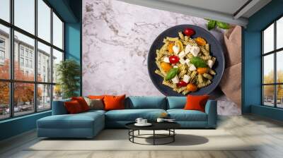 Fresh pesto pasta salad with different colours of cherry tomatoes and mozzarella with a light background. Wall mural