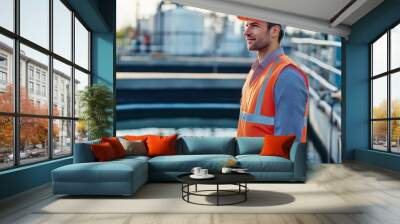 A focused engineer in an orange safety vest and helmet stands by a water treatment facility, overseeing operations with dedication. Wall mural