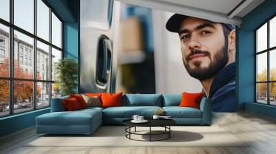 A young man wearing a cap smiles confidently next to a delivery truck, showcasing his role in logistics and transportation. Wall mural