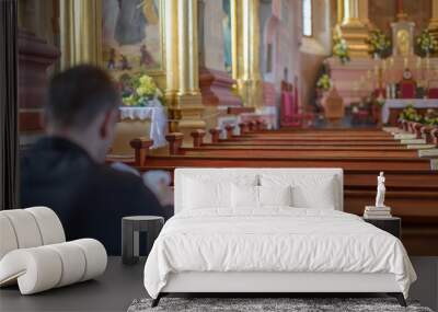 a young man or priest in a black shirt sits on a wooden bench and prays inside the Catholic Church Wall mural