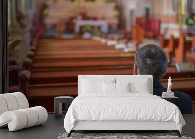 a young man or priest in a black shirt sits on a wooden bench and prays inside the Catholic Church Wall mural