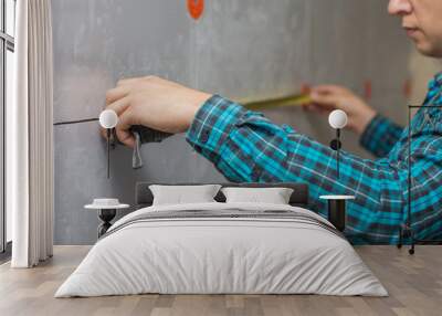 A young working man in a shirt measures with a measuring tape a warmed wall Wall mural