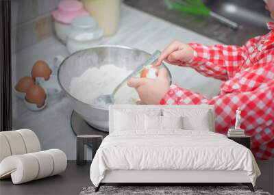 adorable little girl making the dough for pancakes or cookies in the kitchen. A child weighs ingredients for baking on a kitchen scale. Wall mural