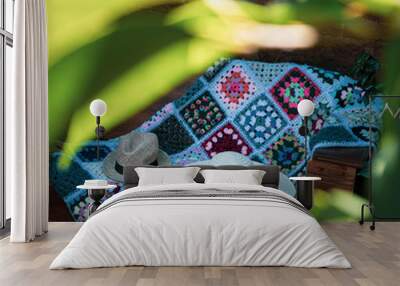 a nice pair of hats and a handmade colorful blanket on a bench in the garden in sunny day Wall mural