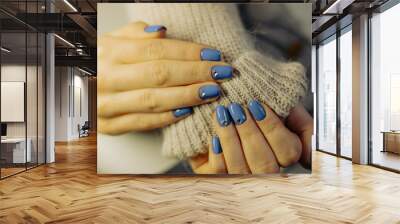 Stylish hands with blue nail polish accentuated by silver studs, wrapped in a cozy knit sweater during a relaxed indoor setting Wall mural