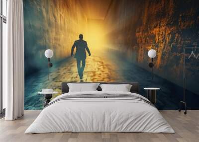 A lone figure walks towards a bright light at the end of a dark, narrow passageway. Wall mural