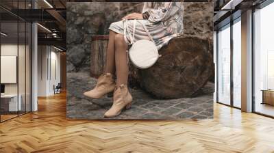 Stylish fashionable woman with trendy leather round white handbag bag. The beige stylish boots are long on a model, against a stone background. fashionable footwear and bag. Wall mural