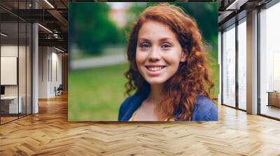 Close-up portrait of beautiful young lady with long red hair and freckles smiling looking at camera in park in summer. Nature, people and happiness concept. Wall mural