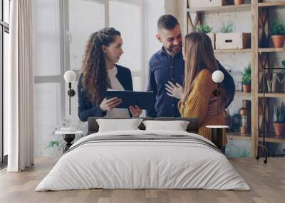 Happy young family is talking to housing agent inside new flat about purchasing real estate, hugging and gesturing emotionally. Moving house and buying property concept. Wall mural