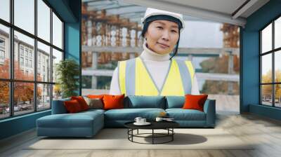 portrait of female builder standing outside construction area wearing safety helmet. People and technical profession concept. Wall mural