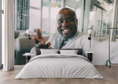 Pov of African American businessman in formal clothes chatting to family on smartphone and waving his hand happily in a classy cafe. He gesticulates actively and cheerfully. Wall mural