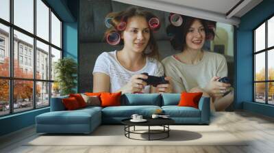 Two funny women play console games with gamepad and have fun at home Wall mural