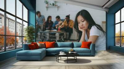 Young asian girl feels upset and isolated while her flatmates celebrating party at home Wall mural