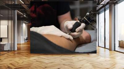 Tattoo artist tattooing a custom design on the inside of a woman ankle Wall mural