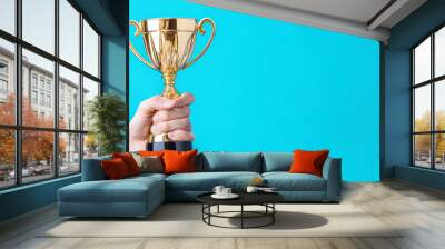 Businessman or boss holding champion golden trophy for winner, success and achievement award in business concept. Man in a suit with a gold trophy prize on blue background. Wall mural