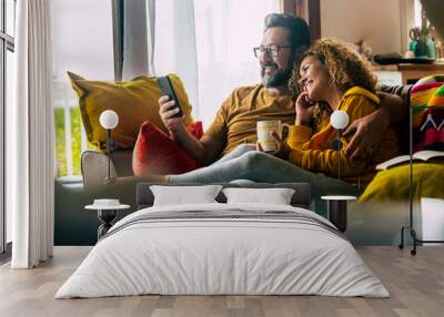 Adult caucasian couple at home enjoy phone call conference with friends - people and technology activity - happy man and woman have breakfast together on the couch Wall mural