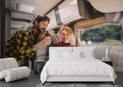 Adult couple enjoy work together using laptop computer sitting inside camper rv vehicle. Concept of nomad and alternative free job lifestyle. Modern man and woman people with technology Wall mural