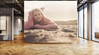 Attractive lady lay down at the beach on the sand in winter or autumn season with a pink sweater enjoying the outdoor relaxed activity alone with no people around -millennial girl feel the world Wall mural