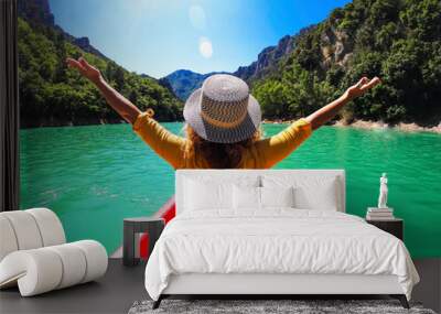 Back view of a woman with hat outstretching arms for happiness sitting on a red canoe kayak in a blue river tour. Outdoor tourist leisure activity on travel vacation Wall mural