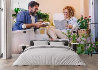 Cheerful couple smile and read book together enjoying terrace at home sitting on white chairs. Adult caucasian people man and woman spend time together in friendship or relationship Wall mural