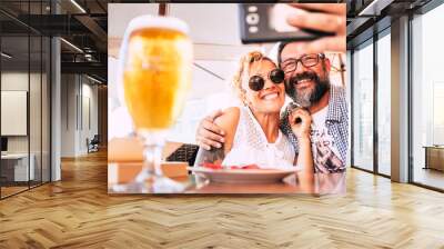 Cheerful happy people couple at the restaurant enjoying and having fun together taking selfie picture with modern phone - hug and relationship love concept for middle age woman and man Wall mural