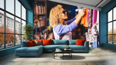 Cheerful traveler young blonde curly woman looking and choosing clothes at the used market during alternative vacation - shopping lifestyle concept for nice people Wall mural