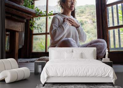 Close-up of calm Caucasian woman holding hands on heart chest and feeling thankful and grateful. Happy female shows gratitude, love and care, she prays or visualizes. Religion, faith concept. Wall mural